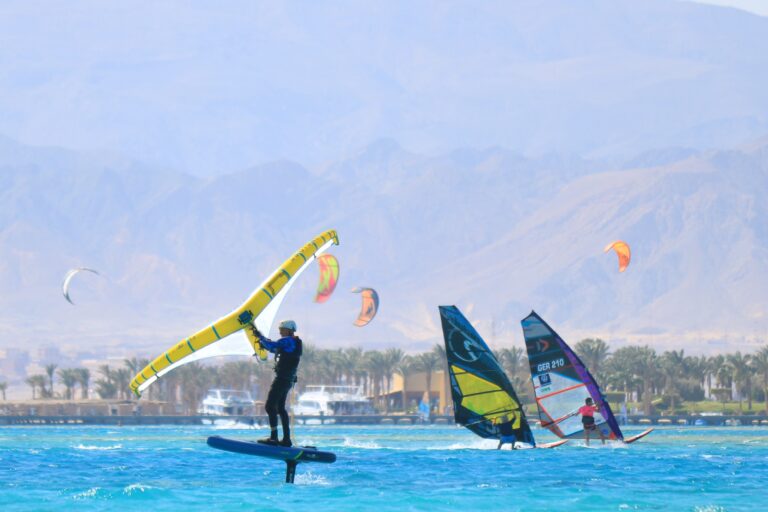 A wing foiler glides over blue water with two windsurfers in the background