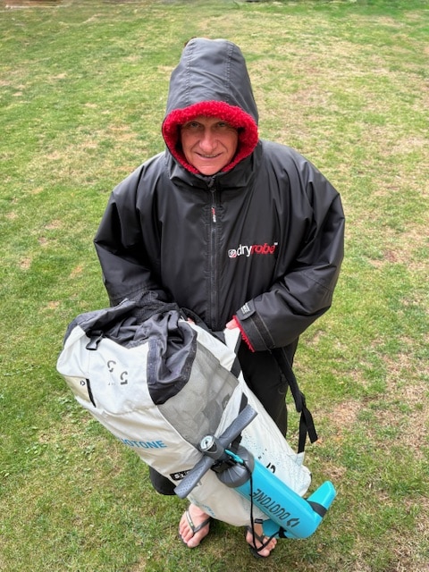A wing foiler all wrapped up in a dryrobe ready to pump up a wing