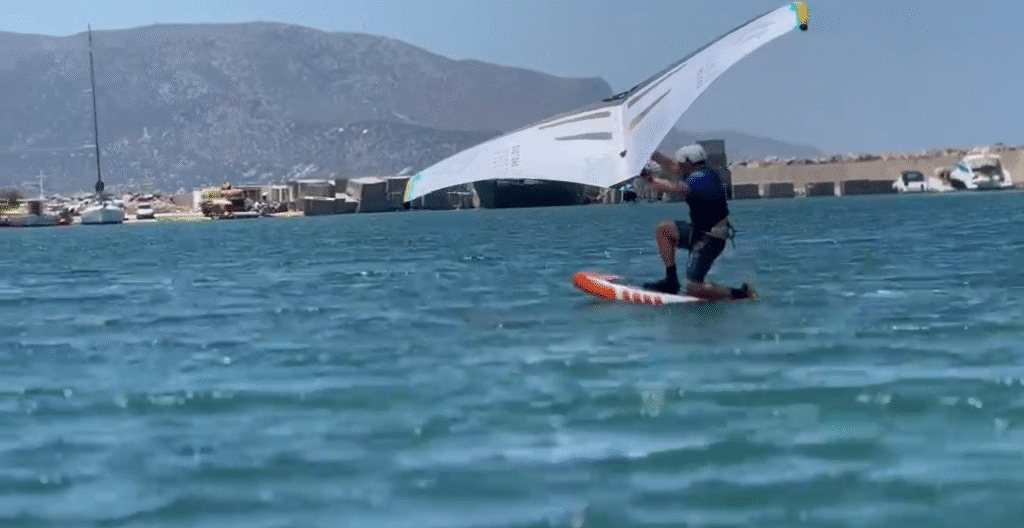 A winger kneeling on the board and getting started in warm blue water