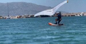 A winger kneeling on the board and getting started in warm blue water
